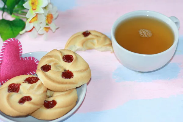 Shortbread com geléia de cereja e coração rosa em um pires, uma caneca de chá em uma mesa de madeira rosa-azul . — Fotografia de Stock