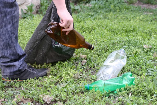 Kot pantolonlu bir adam doğanın ekolojisi ile uğraşır ve zemintemizler plastik bir torba içinde plastik şişe toplar.
