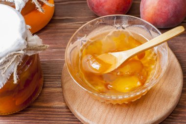 Piala sabah güneşinde masanın üzerinde ahşap yuvarlak standı üzerinde ev yapımı şeftali reçeli bir kaşık ile. Ev yapımı koruma kavramı. Yakın çekim