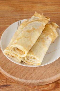 Ahşap bir arka planda bir daire üzerinde haddelenmiş üç lezzetli ev yapımı krep. Sıvı un hamur geleneksel bir çanak. Boşluk Kopyala