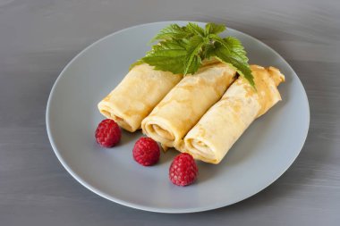 Gri bir doku arka plan üzerinde gri bir tabak üzerinde ahududu ve nane ile birkaç haddelenmiş krep