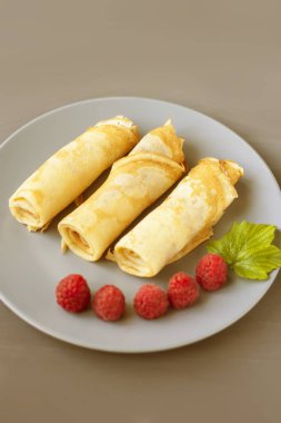 Gri bir doku arka plan üzerinde gri bir tabak üzerinde ahududu ve nane ile birkaç haddelenmiş krep