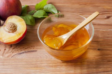 Piala sabah güneşinde masanın üzerinde ahşap yuvarlak standı üzerinde ev yapımı şeftali reçeli bir kaşık ile. Ev yapımı koruma kavramı. Yakın çekim