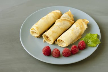 Gri bir doku arka plan üzerinde gri bir tabak üzerinde ahududu ve nane ile birkaç haddelenmiş krep