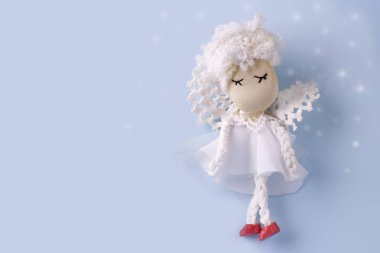 Bokeh ile açık mavi arka planda beyaz giysiler içinde sevimli el yapımı melek ile kartpostal düzeni. Boşluk Kopyala