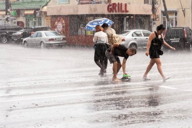 Odessa, Ukrayna, yaz 2019 - Genç adam ayakkabılarını çıkardı ve şiddetli yağmurda yalınayak yolun karşısına geçti.