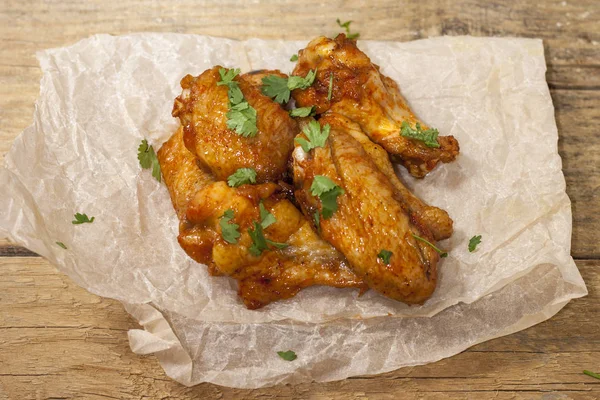 Fried juicy chicken wings marinated with honey, soy sauce, spices, sprinkled with finely chopped cilantro on a paper background. Asian recipe, top view, close-up.