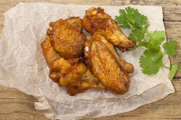 Fried juicy chicken wings marinated with honey, soy sauce, spices with a cilantro branch on a paper background. Asian recipe, top view, close-up. — Stock Photo, Image