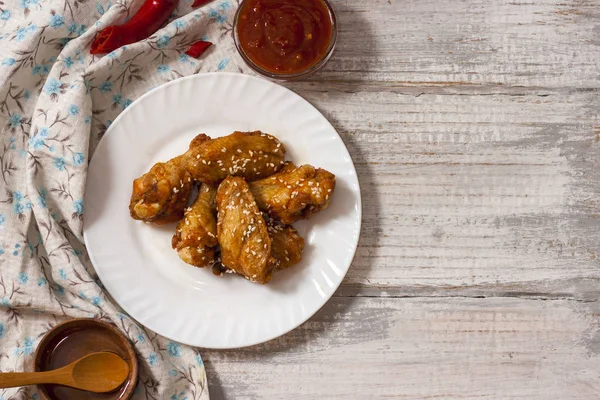 Fried juicy chicken wings marinated with honey, soy sauce, spices, sprinkled with sesame seeds on a white plate with sauce. Asian recipe, top view, close up. Copy space