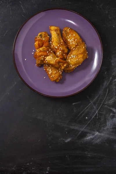 Τηγανητά ζουμερά φτερά κοτόπουλου μαριναρισμένα με μέλι, σάλτσα σόγιας, μπαχαρικά, ψεκάζονται με σουσάμι σε ένα πιάτο σε μαύρο φόντο. Ασιατική συνταγή, κορυφή θέα — Φωτογραφία Αρχείου