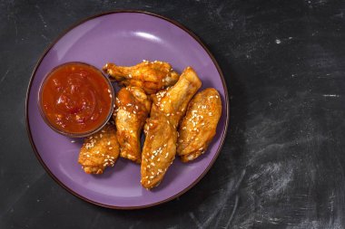 Kızarmış sulu tavuk kanatları bal, soya sosu, baharat, biber soslu siyah bir arka plan üzerinde bir tabak üzerine susam serpilir marine. Asya tarifi, üst tesbil