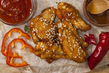 Kızarmış sulu tavuk kanatları bal, soya sosu, baharat, ahşap bir arka plan üzerinde kağıt üzerine susam serpilir marine. Asya tarifi, üstte, yakından