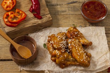 Kızarmış sulu tavuk kanatları bal, soya sosu, baharat, ahşap bir arka plan üzerinde kağıt üzerine susam serpilir marine. Asya tarifi, üstte, yakından