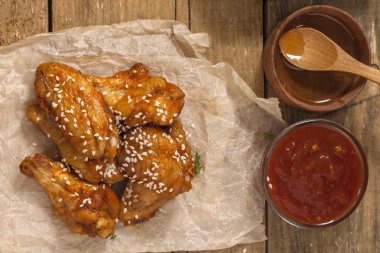 Kızarmış sulu tavuk kanatları bal, soya sosu, baharat, ahşap bir arka plan üzerinde kağıt üzerine susam serpilir marine. Asya tarifi, üstte, yakından