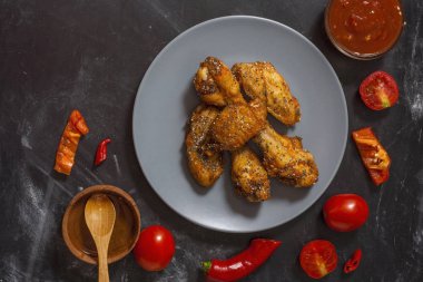 Kızarmış sulu tavuk kanatları bal, soya sosu, baharat, domates, kırmızı biber, bal ve biber sosu ile siyah bir arka plan üzerinde bir tabak üzerinde chia tohumu serpilir marine. Asya tarifi, üst tesbil.