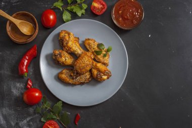 Kızarmış sulu tavuk kanatları bal, soya sosu, baharat, domates, kırmızı biber, bal ve biber sosu ile siyah bir arka plan üzerinde bir tabak üzerinde chia tohumu serpilir marine. Asya tarifi, üst tesbil.