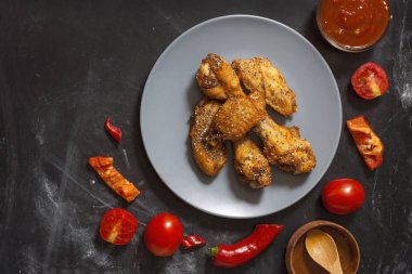 Kızarmış sulu tavuk kanatları bal, soya sosu, baharat, domates, kırmızı biber, bal ve biber sosu ile siyah bir arka plan üzerinde bir tabak üzerinde chia tohumu serpilir marine. Asya tarifi, üst tesbil.