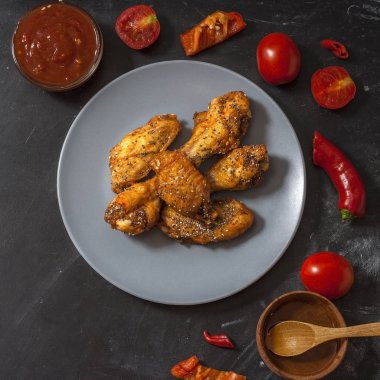 Kızarmış sulu tavuk kanatları bal, soya sosu, baharat, domates, kırmızı biber, bal ve biber sosu ile siyah bir arka plan üzerinde bir tabak üzerinde chia tohumu serpilir marine. Asya tarifi, üst tesbil.