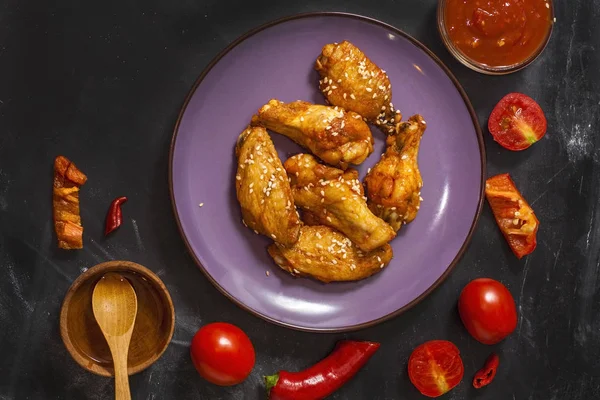Kızarmış sulu tavuk kanatları bal, soya sosu, baharat, domates, kırmızı biber, bal ve biber sosu ile siyah bir arka plan üzerinde bir tabak üzerine susam serpilir marine. Asya tarifi, üst tesbil