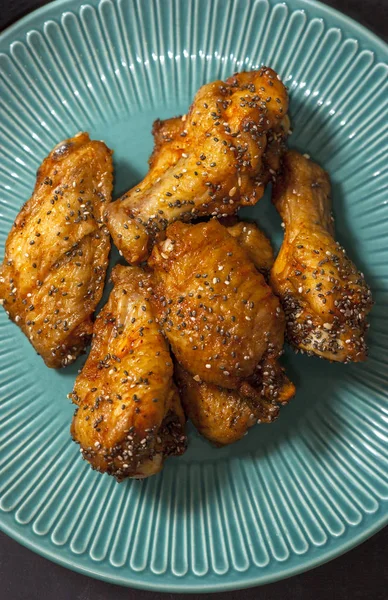 Τηγανητά ζουμερά φτερά κοτόπουλου μαριναρισμένα με μέλι, σάλτσα σόγιας, μπαχαρικά, ψεκάζονται με σπόρους Chia σε ένα πιάτο σε μαύρο φόντο. Ασιατική συνταγή, κορυφή θέα. — Φωτογραφία Αρχείου