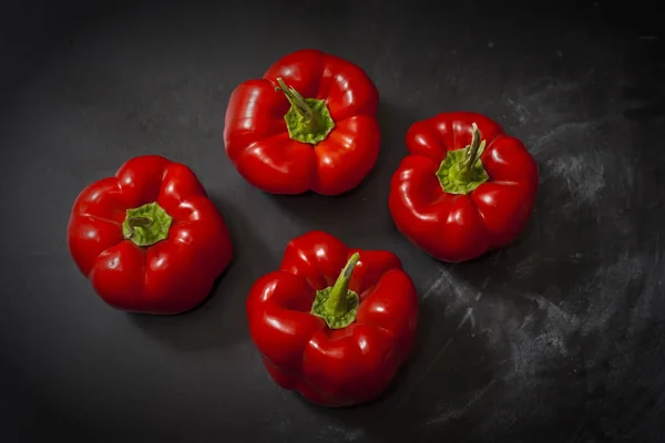 Φρέσκες τέσσερις κόκκινες πιπεριές σε μαύρο φόντο στο κέντρο του πλαισίου. — Φωτογραφία Αρχείου