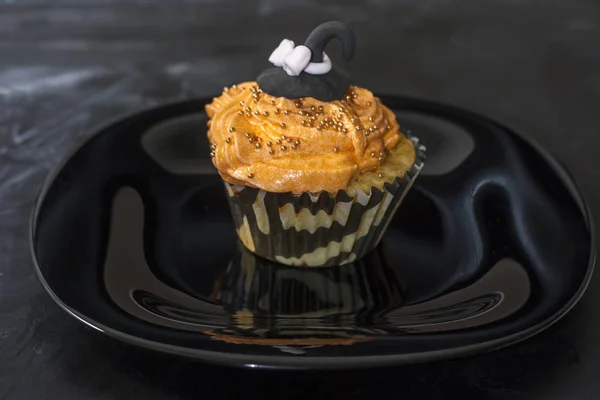 Fröhliche halloween orange und schwarz dekorierte Cupcake mit einem schwarzen Hexenhut und Buttercreme mit Perlen auf einem schwarzen Teller. — Stockfoto