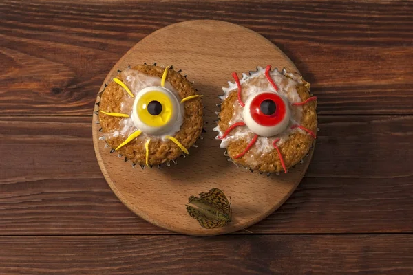 Tasty treat for Halloween dessert, cupcakes with eyes made of sweets on a wooden background.