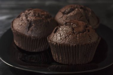 Karanlık bir arka plan üzerinde siyah bir tabak üzerinde üç çikolatalı kekler yakın