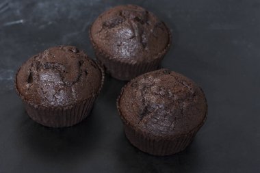 Karanlık bir arka plan üzerinde siyah bir tabak üzerinde üç çikolatalı kekler yakın