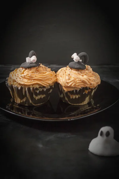 Feliz Halloween naranja y cupcake negro decorado con un sombrero de bruja negro y crema de mantequilla con cuentas en un plato negro . — Foto de Stock