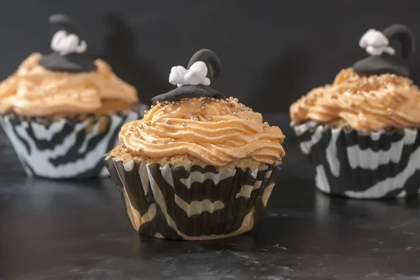 Feliz Halloween naranja y cupcake negro decorado con un sombrero de bruja negro y crema de mantequilla con cuentas sobre un fondo negro — Foto de Stock