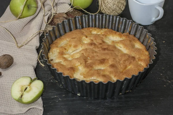Μήλο πίτα Charlotte σε ένα μαύρο ξύλινο τραπέζι με πράσινα μήλα σε μορφή σιδήρου. — Φωτογραφία Αρχείου
