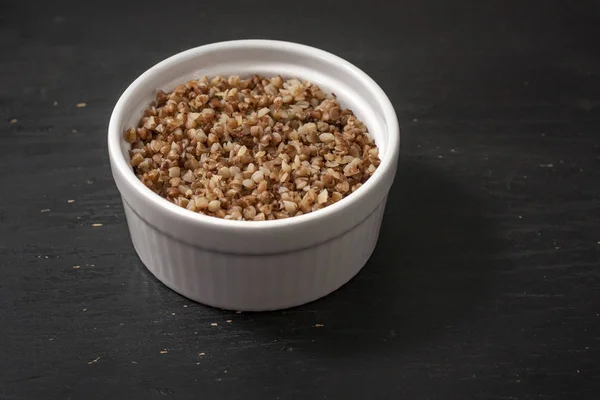 Cooked buckwheat porridge in a deep plate on a black wooden background. Copy space. — Stock Photo, Image