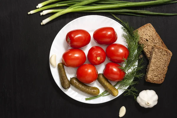 Nourriture fermentée sur une assiette blanche sur une table en bois noir. Tomates marinées et concombres. Du sel pour l'hiver. Snack traditionnel pour l'alcool . — Photo