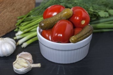 Siyah ahşap bir masada beyaz bir tabakta mayalanmış yemek. Salatalık ve domates turşusu. Kış için tuz. Alkol için geleneksel atıştırma.