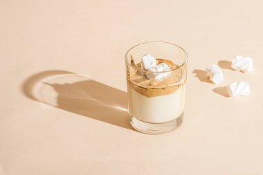 Şeffaf bir bardakta şeffaf bir Dalgon kahvesi ve pastel arka planda kremayla birlikte süt..
