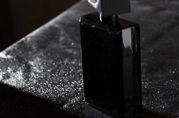 Totaly black bottle of masculine elegent fragrance on black leather background 