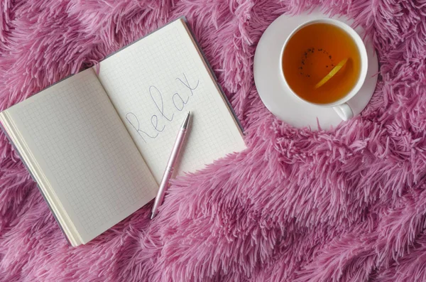 Top view of notebook and word Relax wtitting on it,pen,cup of tea on pink background