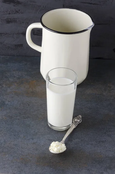 豆腐チーズ 乳白色の製品 暗いテーブルの上のミルク水差しでガラスのスプーン 垂直写真 — ストック写真