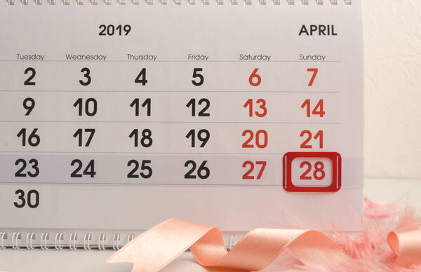 Closeup of calendar with red mark on Easter Day,ribbon and feathers.Concept of preparation foe Easter celebration