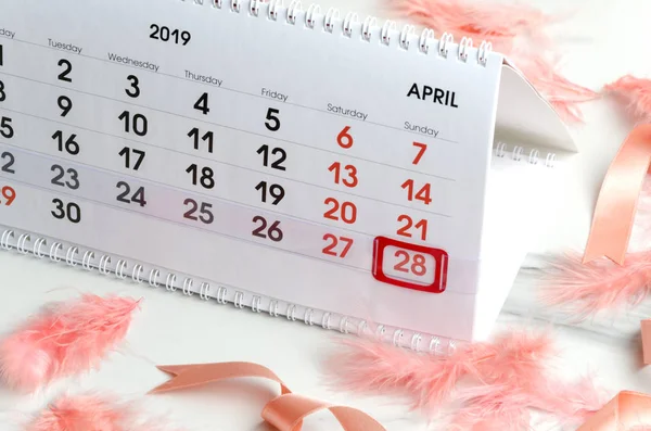 Preparation for Easter holiday.Calendar,coral color featgers and ribbon on white table