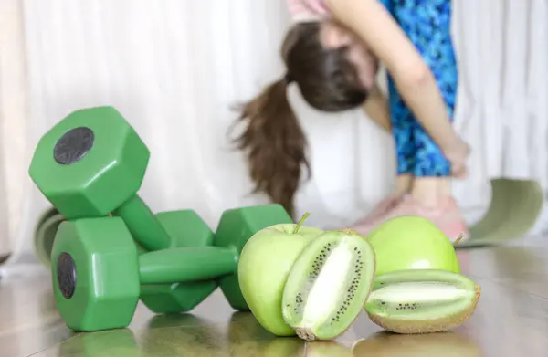 Dumbbells, fresh green fruits and woman doing stretching poses.Concept of healthy and sporty life