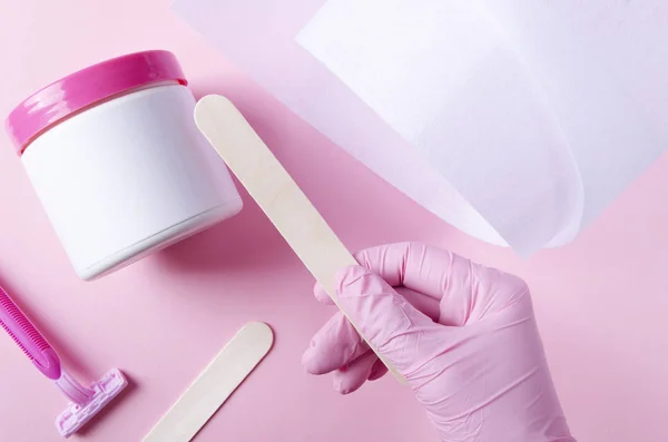 ホットワックスを適用するためにスティックを取るピンクの手袋の美容師 ホットワックス処理の概念 美容ワックスツールのトップビュー — ストック写真