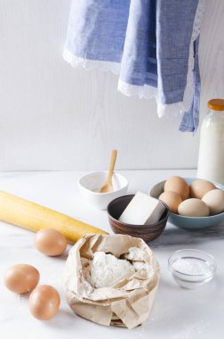 Dikey atış. Pişirme için farklı bileşenler. Un, yumurta, süt, mutfak masasında maya ve duvarda asılı bir önlük. Mutfakta sabah