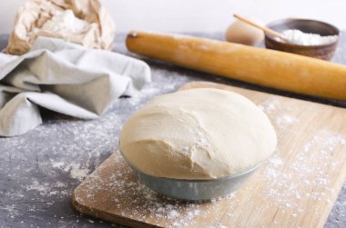 Pişirme işlemi kavramı. Ahşap kesme tahtası üzerinde kase taze hamur Closeup, gri mutfak masasında hamur yapmak için çeşitli malzemeler