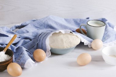 Hazırlanan ekmek veya pizza hamuru, kasede un, yumurta, süt fincan, tuz hazırlanması. Mutfak masasında önlük altında risen hamur
