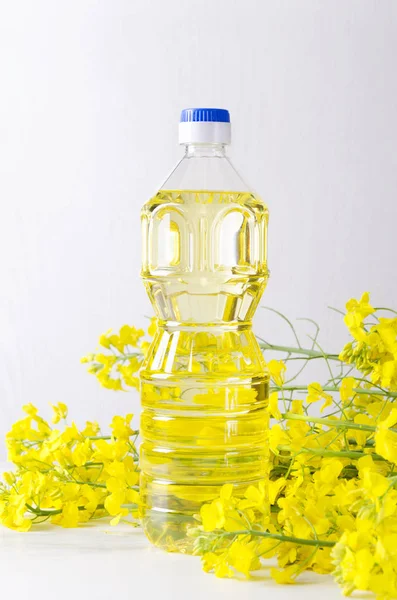 Vertical shot of bottle of canola oil. Rapeseed oil in the plastic bottle and picked blooming canola flowers