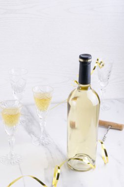 Kutlama partisi kavramı. Şarap şişesi, tam ve boş bardaklar, parlak arka plana karşı beyaz masada tatil dekorasyonu