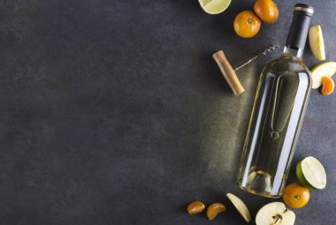 Koyu renkler, parlayan ışıklar. Rustik yüzeyde lezzetli ve sulu meyve ile çevrili beyaz şarap şişesi. Metin için üst görünüm ve boş alan