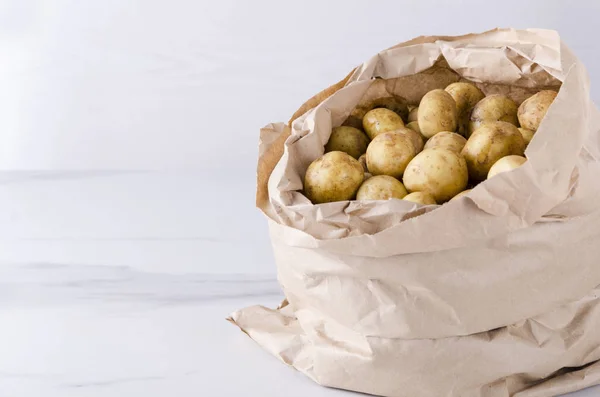 Fresh spring harvest.Paper bag with raw new potatoes on the white surfac.Empty space for text